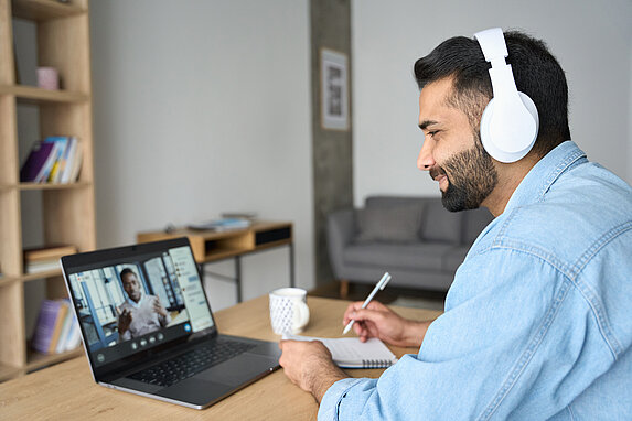 © Getty Images. Ein Mann sitzt mit Kopfhörern vor einem Laptop.