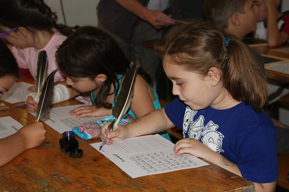 Mehrere Kinder schreiben mit Schreibfedern.