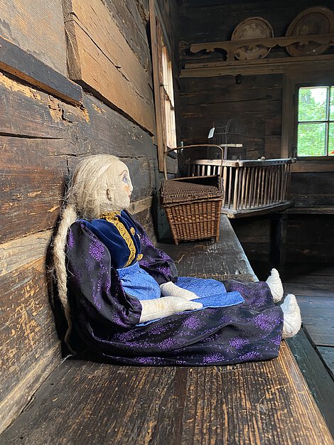 Eine Puppe im blauen Kleid auf einer Holzbank.